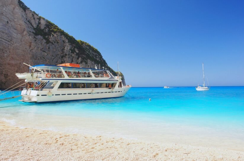 A Boat Rests On The Sandy Shores Of Navagio Beach In Zakynthos, Surrounded By Turquoise Waters And Steep Cliffs