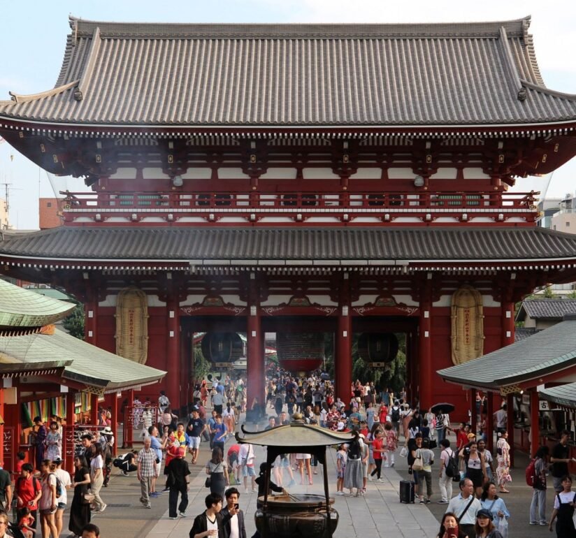 A Large Red Sensoji Temple In Japan, Surrounded By Many Visitors Walking Around The Area