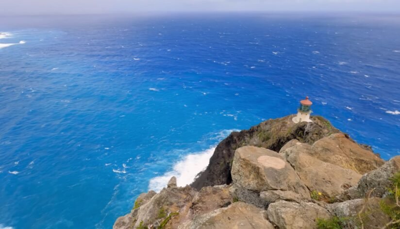 A Lighthouse Atop A Cliff At Makapuʻu Point, Overlooking The Vast Ocean Under A Clear Blue Sky