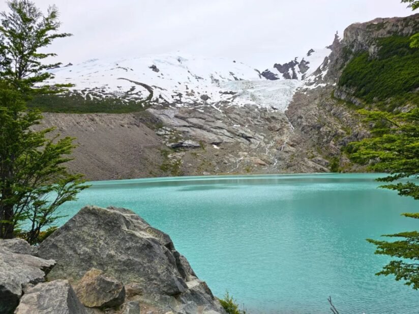 A Serene Lake With The Huemul Glacier Towering In The Background, Showcasing The Beauty Of Nature During A Hike