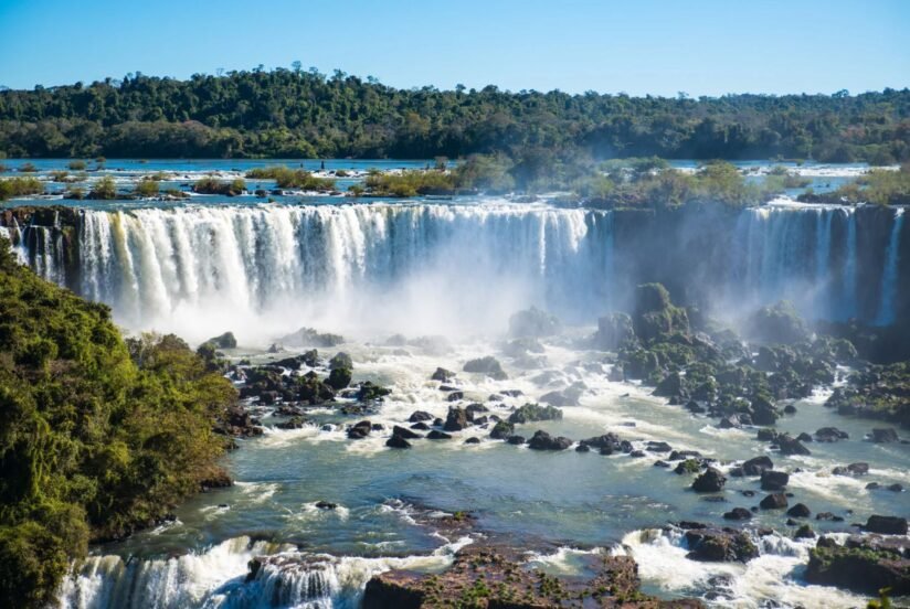 Iguazu Falls In Brazil, Displaying Dramatic Waterfalls Plunging Into A River, Framed By Rich Vegetation And Misty Air