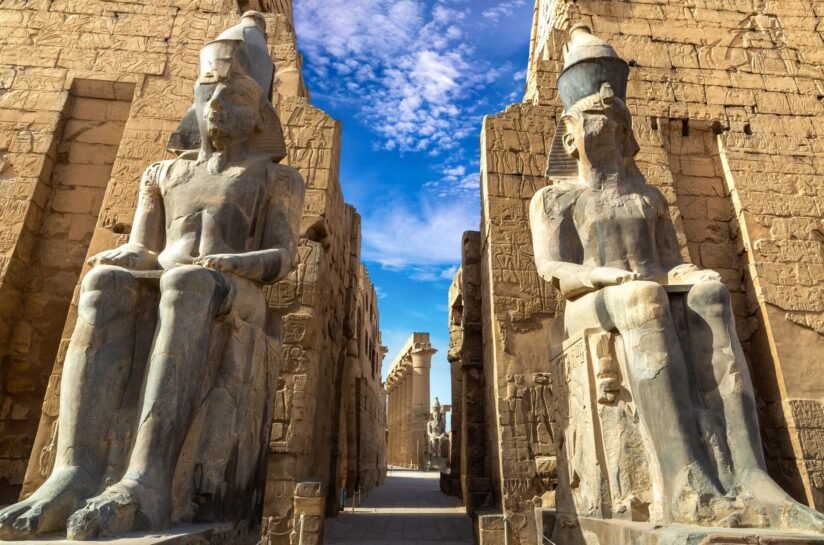 Statues Of Egyptian Gods Stand In Front Of A Clear Blue Sky At Luxor Temple, Egypt